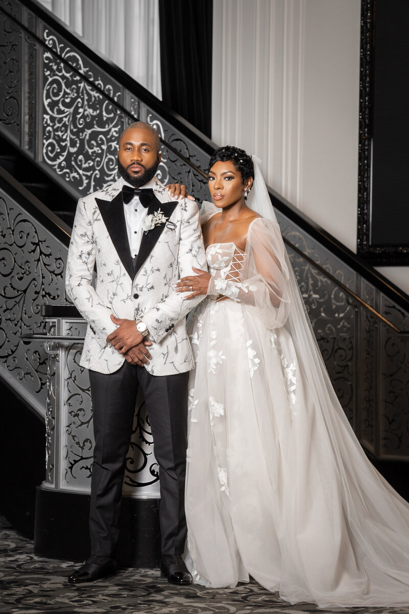 Bride and groom posing beside an ornate black staircase